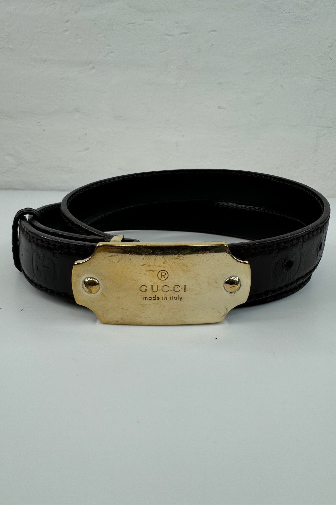 Sort Gucci bælte i glat læder, guldspænde med "GUCCI" og "made in Italy", syninger langs kanten.