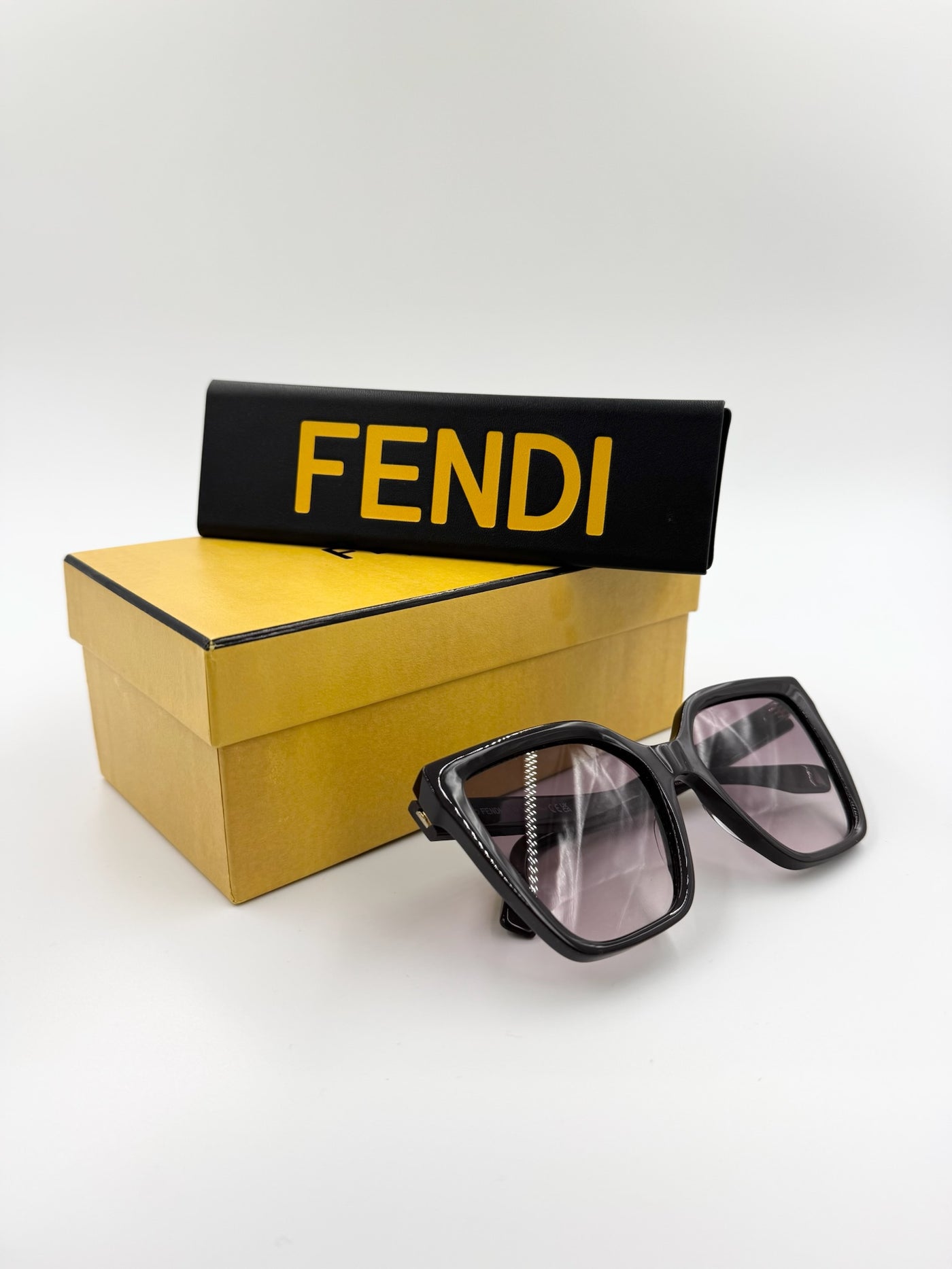 Sorte, firkantede solbriller, gul æske, sort etui med "FENDI" i gul tekst.