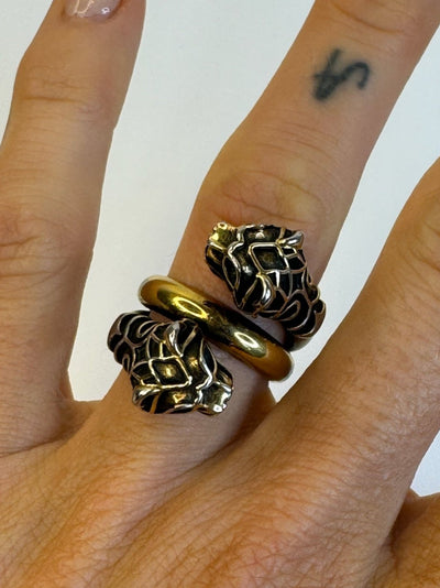 Dobbelt viklet ring med tigerhoveder og skinnende metalfinish, båret på en finger.