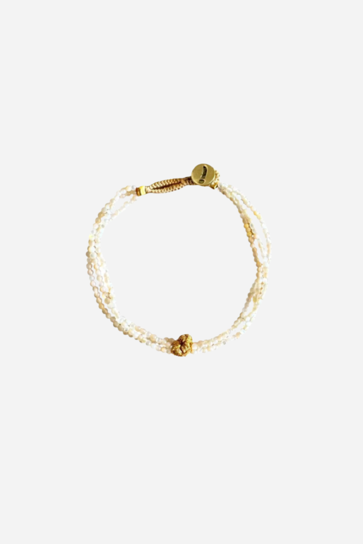 Armbånd med hvide perler i flere strenge, guldfarvet knude i midten og rund guldlås.