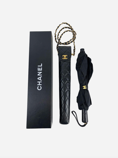 Sort Chanel paraply med quiltet etui og guldkæde, ved siden af en sort Chanel æske.