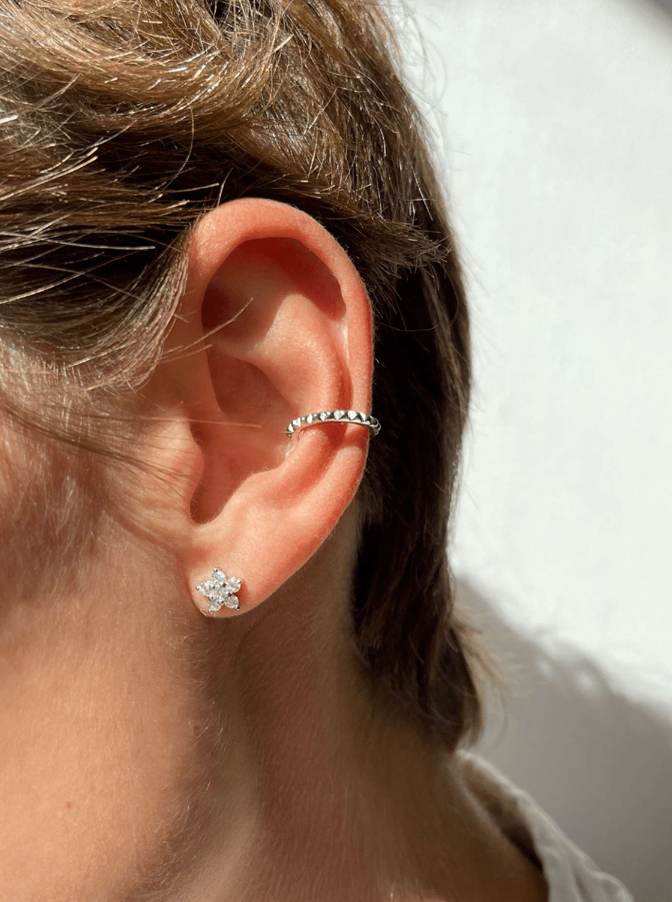 Øre med to øreringe; en blomst med glitrende sten og en enkel, mønstret hoop.